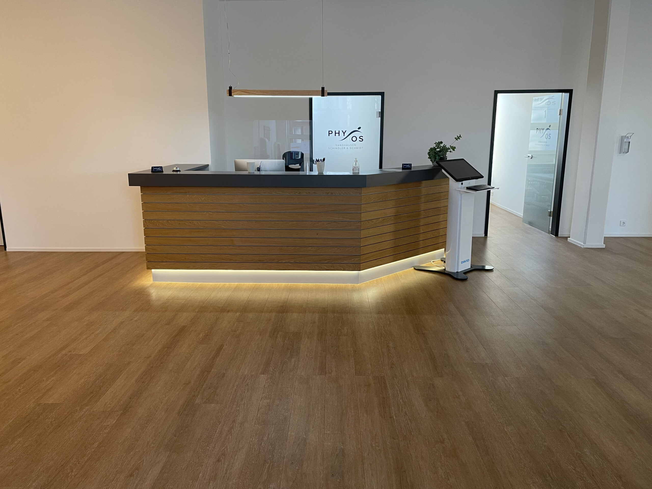Empfangstresen aus Holz mit Physios-Logo auf der Glaswand